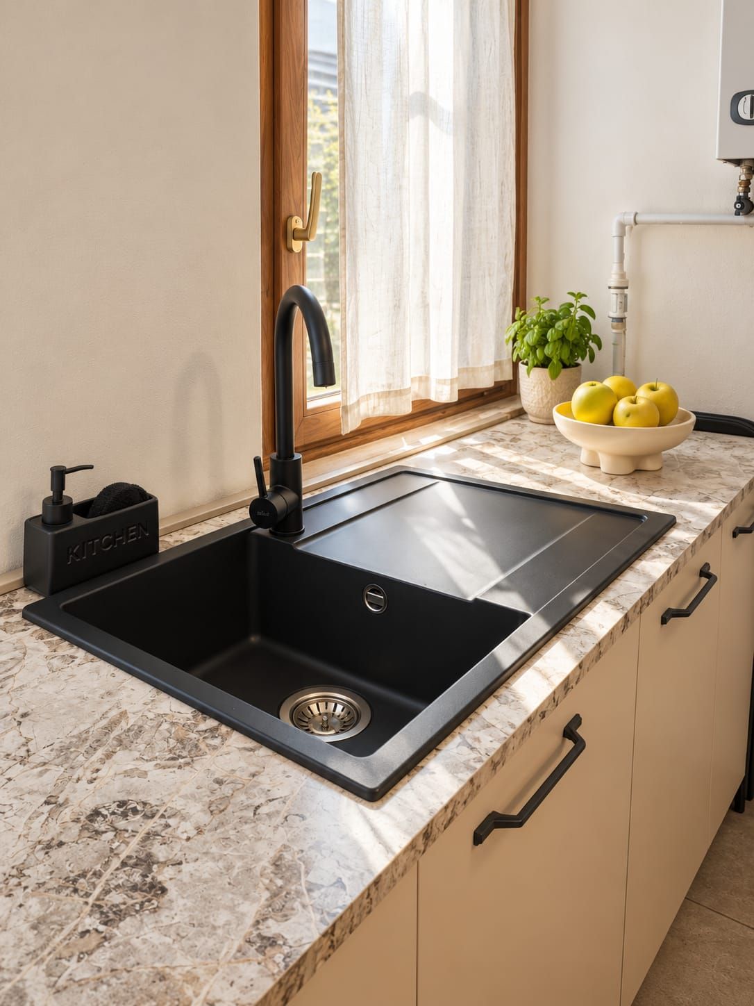 Une cuisine avec un évier noir, un robinet, un saladier rempli de citrons et une plante en pot.