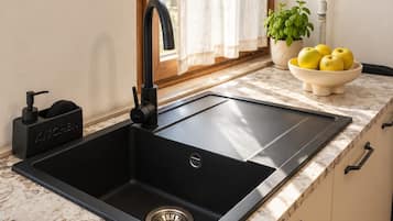 A kitchen with a black sink, a faucet, a bowl of lemons, and a potted plant.