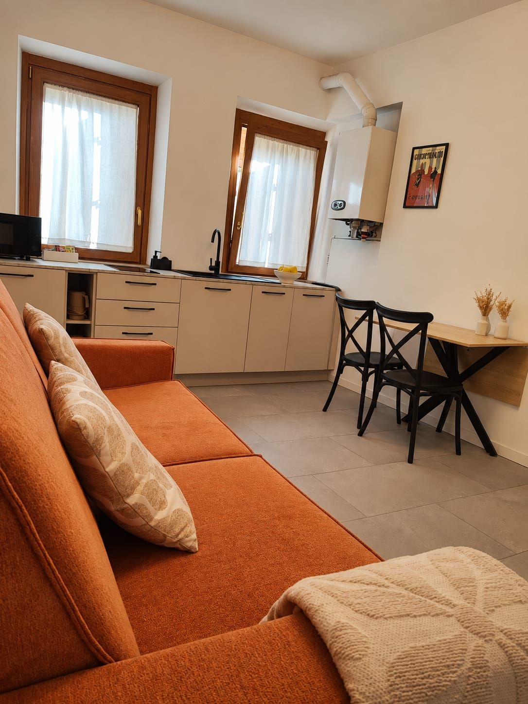 A compact living space with a sofa, a dining table with chairs, a kitchen area, and a window with curtains.