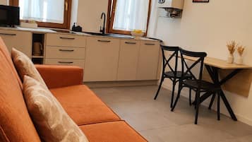 A compact living space with a sofa, a dining table with chairs, a kitchen area, and a window with curtains.