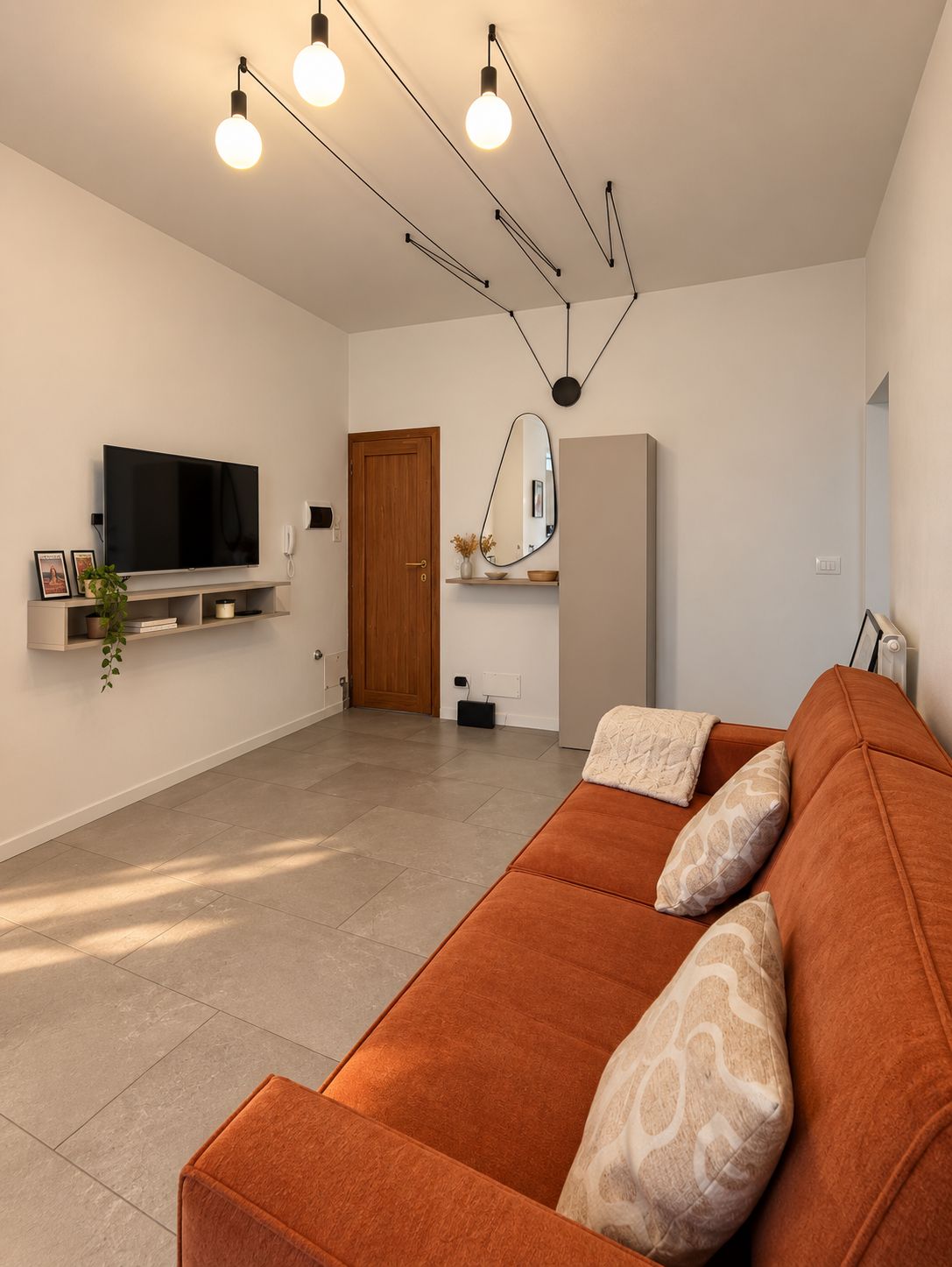 Un salon moderne avec un grand canapé orange, un téléviseur à écran plat fixé au mur et un design minimaliste agrémenté d’une porte en bois et d’un miroir.