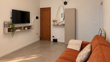 A modern living room with a large orange sofa, a flat-screen TV mounted on the wall, and a minimalist design with a wooden door and a mirror.