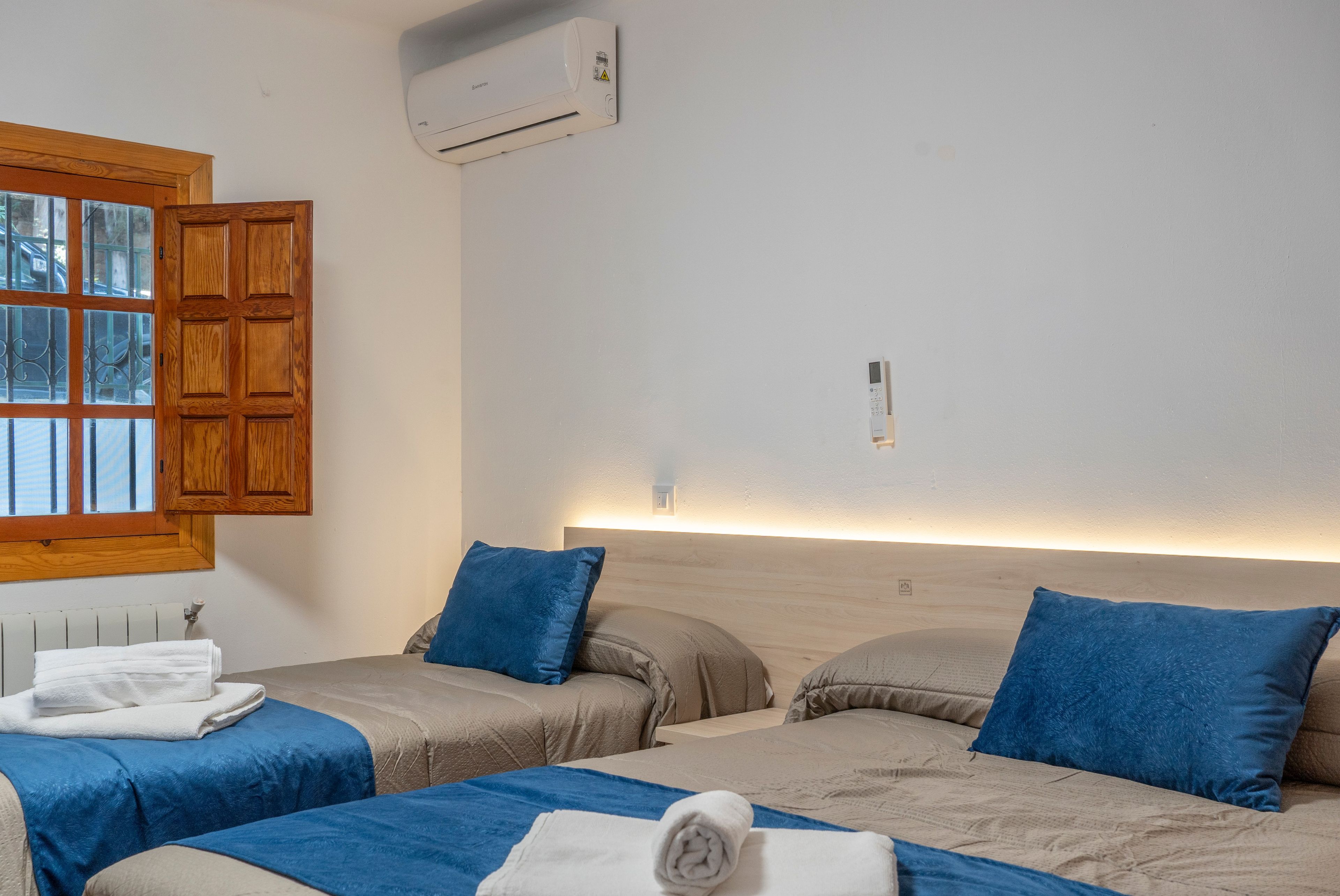 Ein Hotelzimmer mit zwei Betten, einem Fenster mit Holzjalousien, einer Klimaanlage und einem Nachttisch mit Lampe.