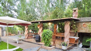 An outdoor patio area with a stone floor, a brick barbecue station, and a seating area with a table and chairs.