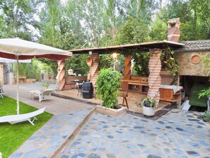 Un área de patio exterior con piso de piedra, una estación de barbacoa de ladrillo y un espacio de estar con mesa y sillas.