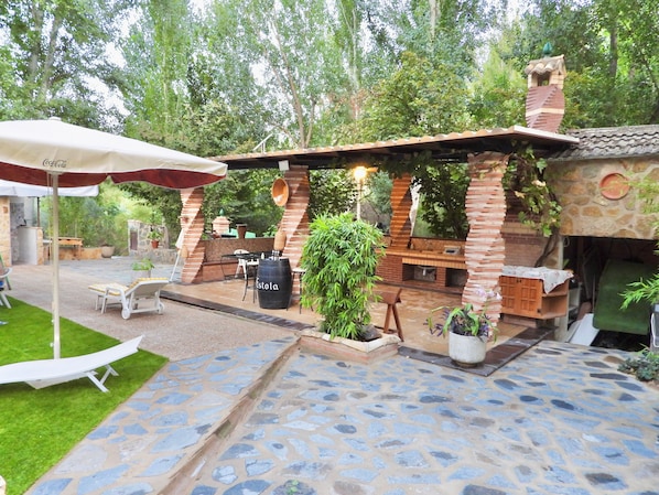 Zona de pati exterior amb sòl de pedra, una estació de barbacoa de maó i un espai d'estar amb taula i cadires.