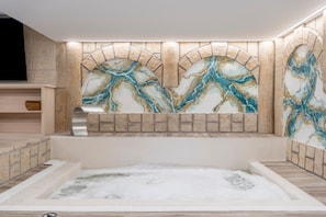 A spa area with a marble wall, a bathtub, and a wooden shelf.