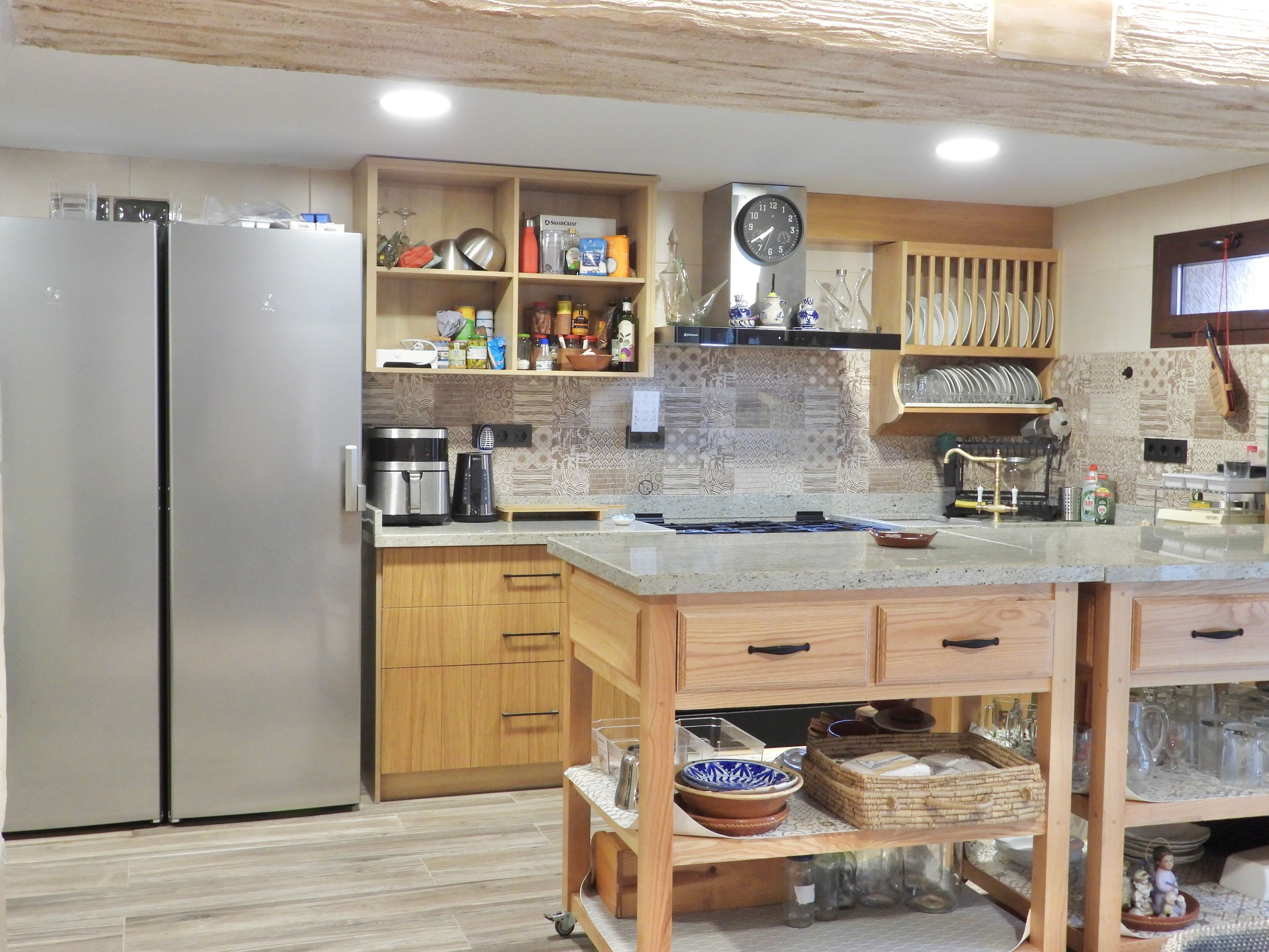 Una cocina moderna con un refrigerador de acero inoxidable, armarios de madera, una estufa integrada y diversos electrodomésticos.
