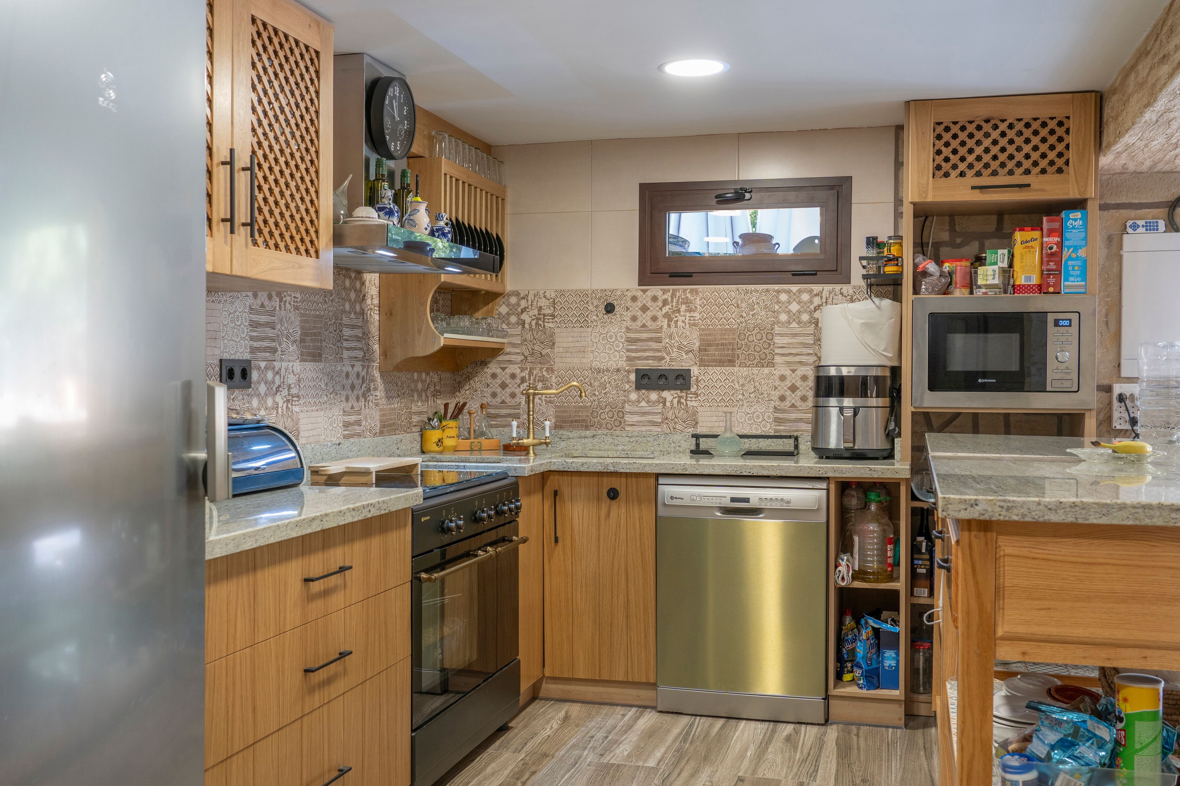 Una cocina moderna con armarios de madera, lavavajillas de acero inoxidable, horno empotrado y microondas.