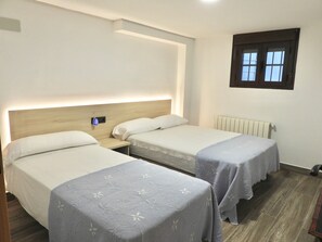Habitació d'hotel amb dos llits individuals, una tauleta de nit, un escalfador fixat a la paret i una finestra amb persianes.