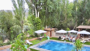 A swimming pool with lounge chairs and umbrellas, surrounded by greenery and a stone wall.