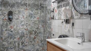 Un baño con baldosas de estampado floral, un lavabo blanco, un cabezal de ducha de mano y un secador de pelo montado en la pared.