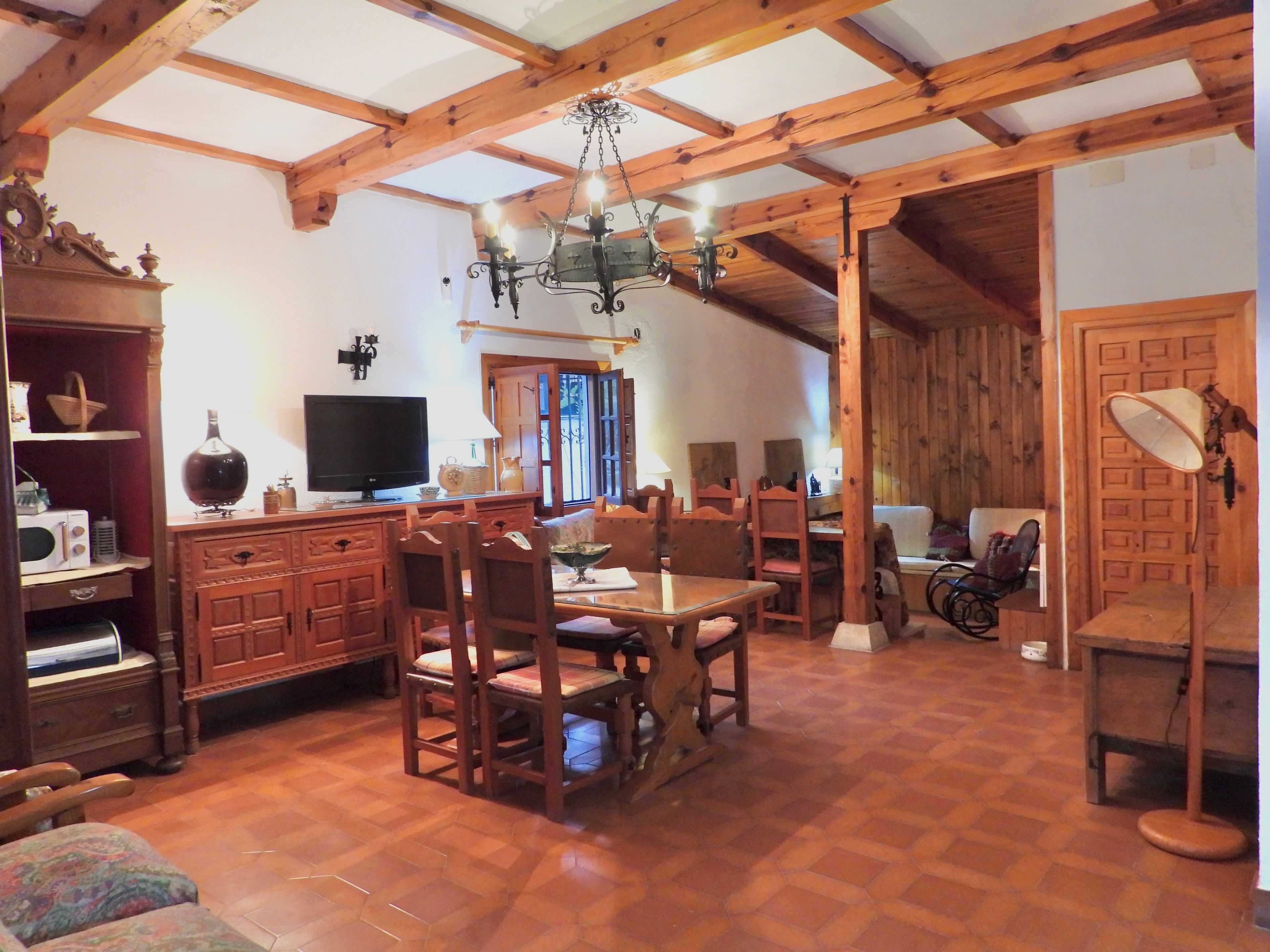 Un interior rústico con una mesa de comedor de madera, sillas, un televisor y una araña.