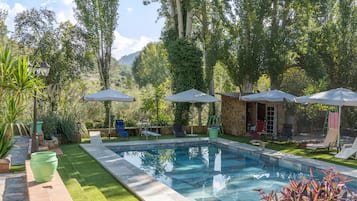 Une piscine entourée de verdure et de murs en pierre, avec des chaises longues et des parasols.