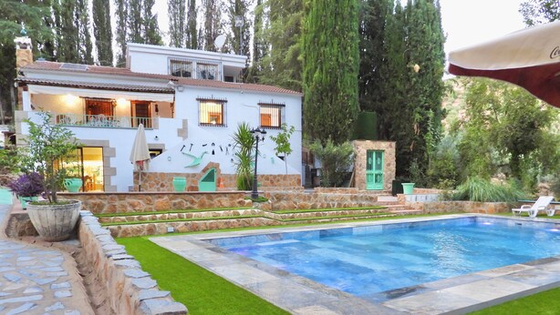 A swimming pool with a stone border, a stone wall, and a well-maintained lawn.