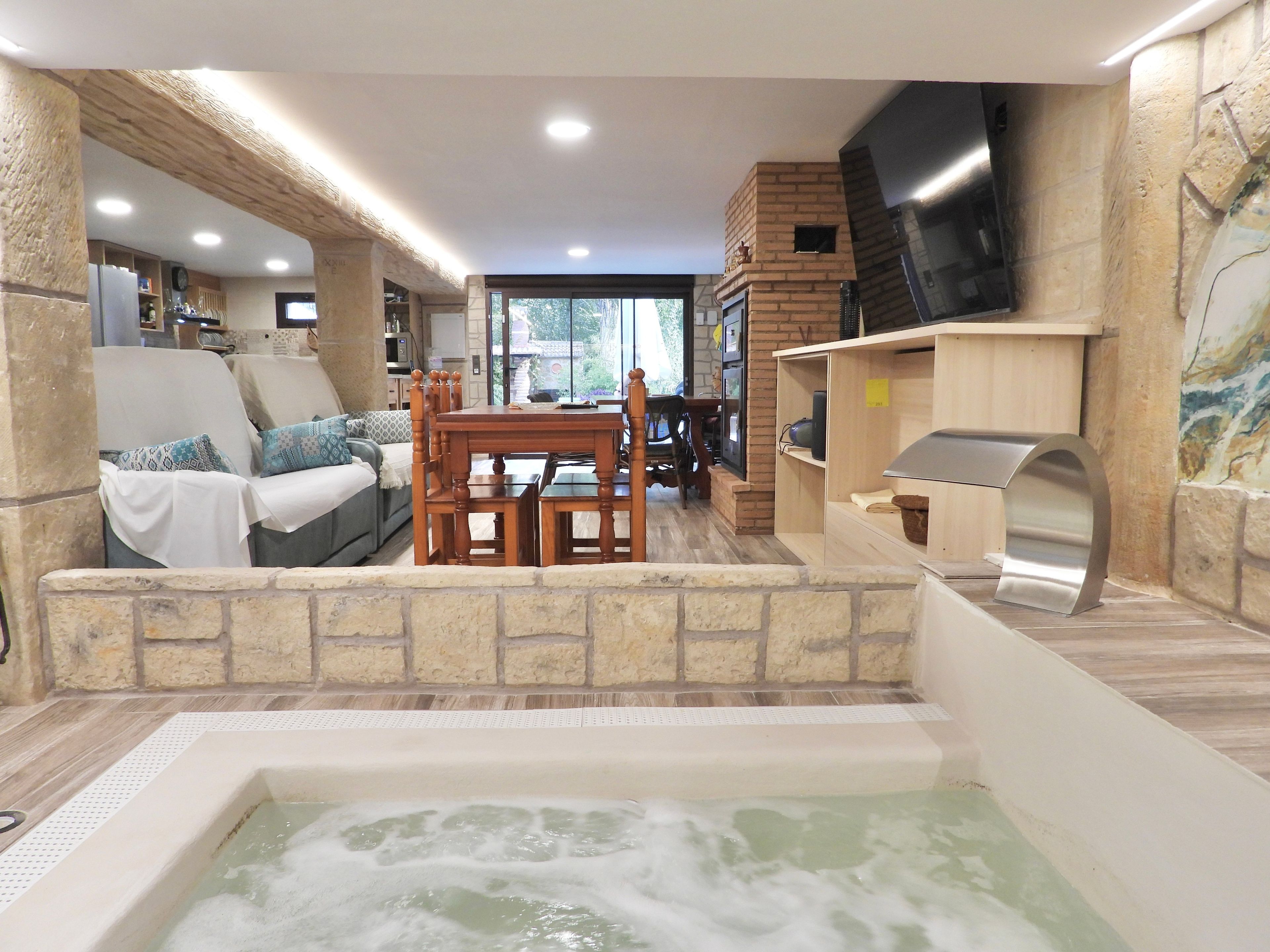 Un área de spa con un jacuzzi, mobiliario de madera, paredes de piedra y un televisor.