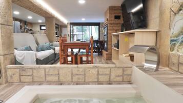 Un área de spa con un jacuzzi, mobiliario de madera, paredes de piedra y un televisor.