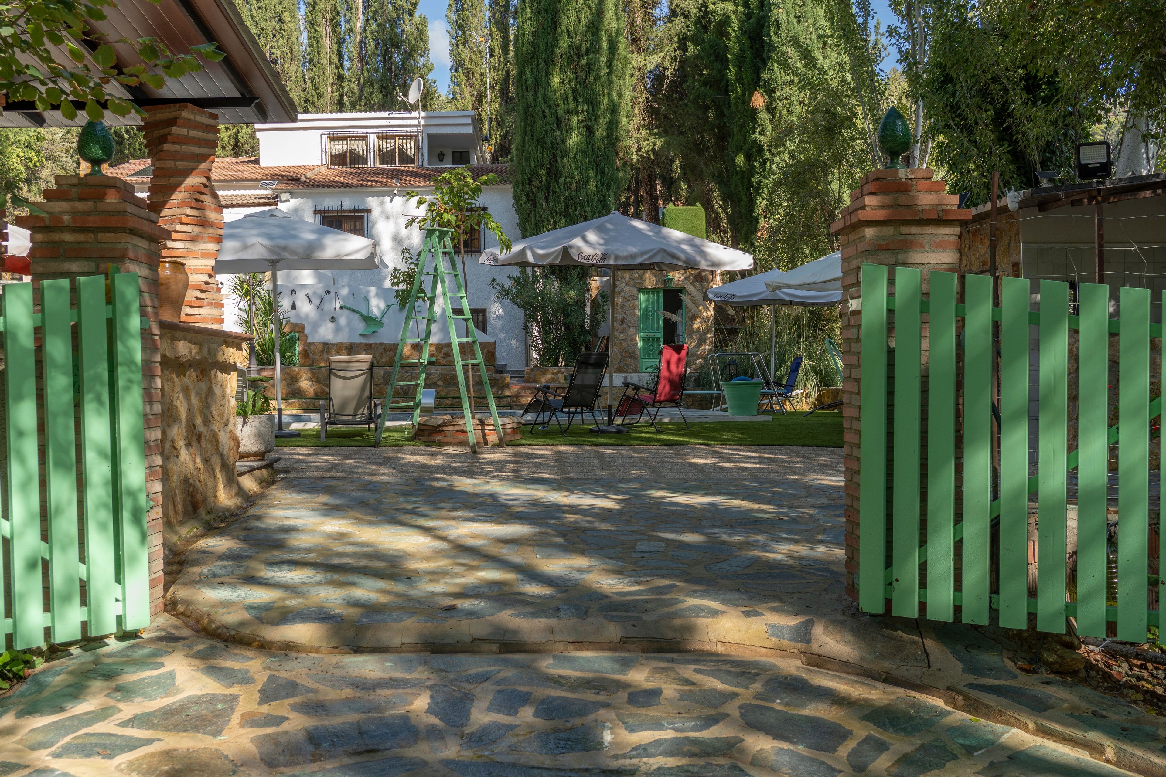 Un chemin de pierre mène à une entrée fermée par un portail, d’où l’on aperçoit un espace patio.