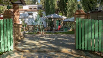 Un chemin de pierre mène à une entrée fermée par un portail, d’où l’on aperçoit un espace patio.