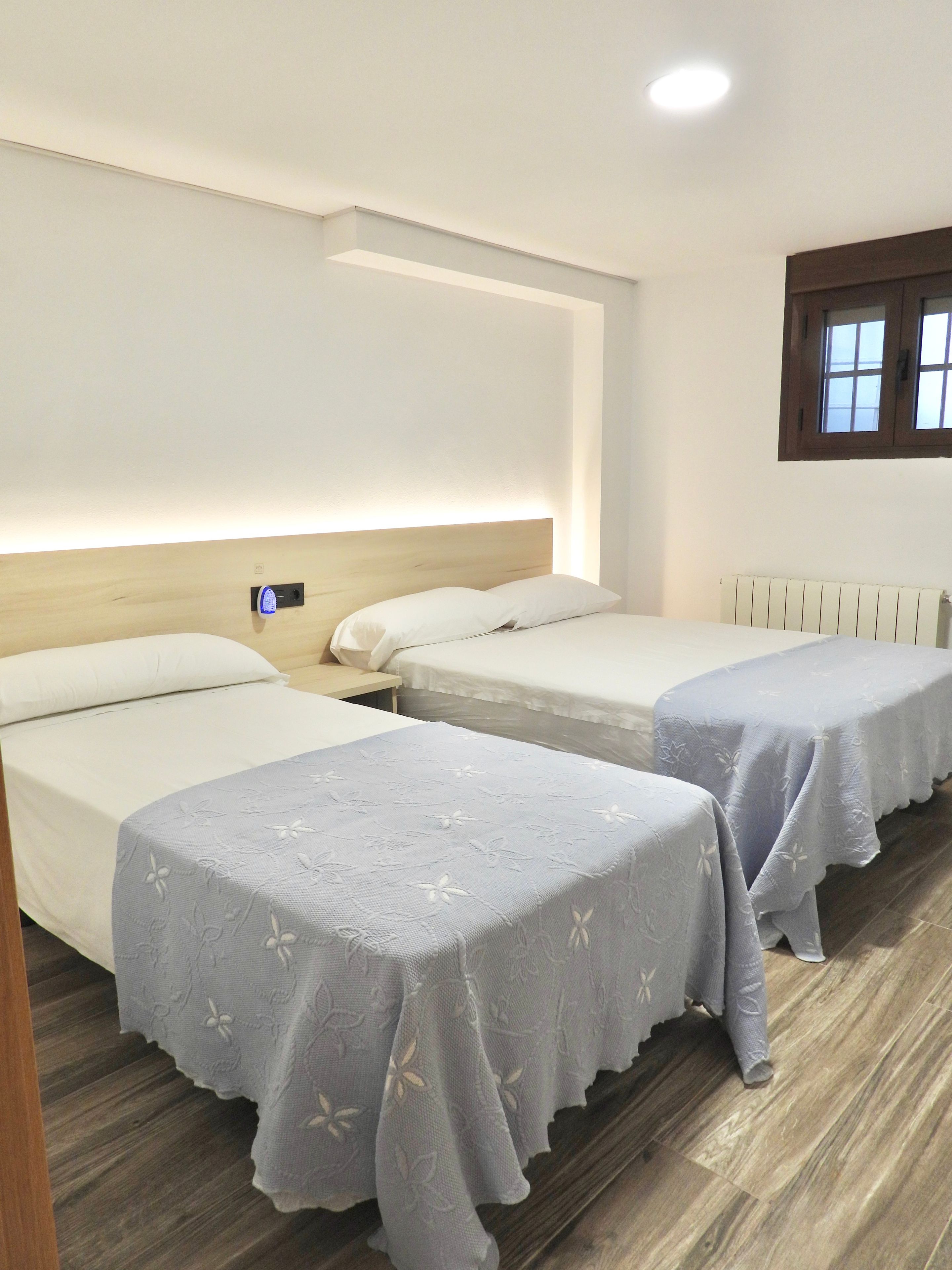 Habitación de hotel con dos camas individuales, un cabecero de madera, un radiador blanco y una ventana con vistas.