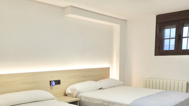 Quarto de hotel com duas camas de solteiro, cabeceira de madeira, radiador branco e janela com vista.