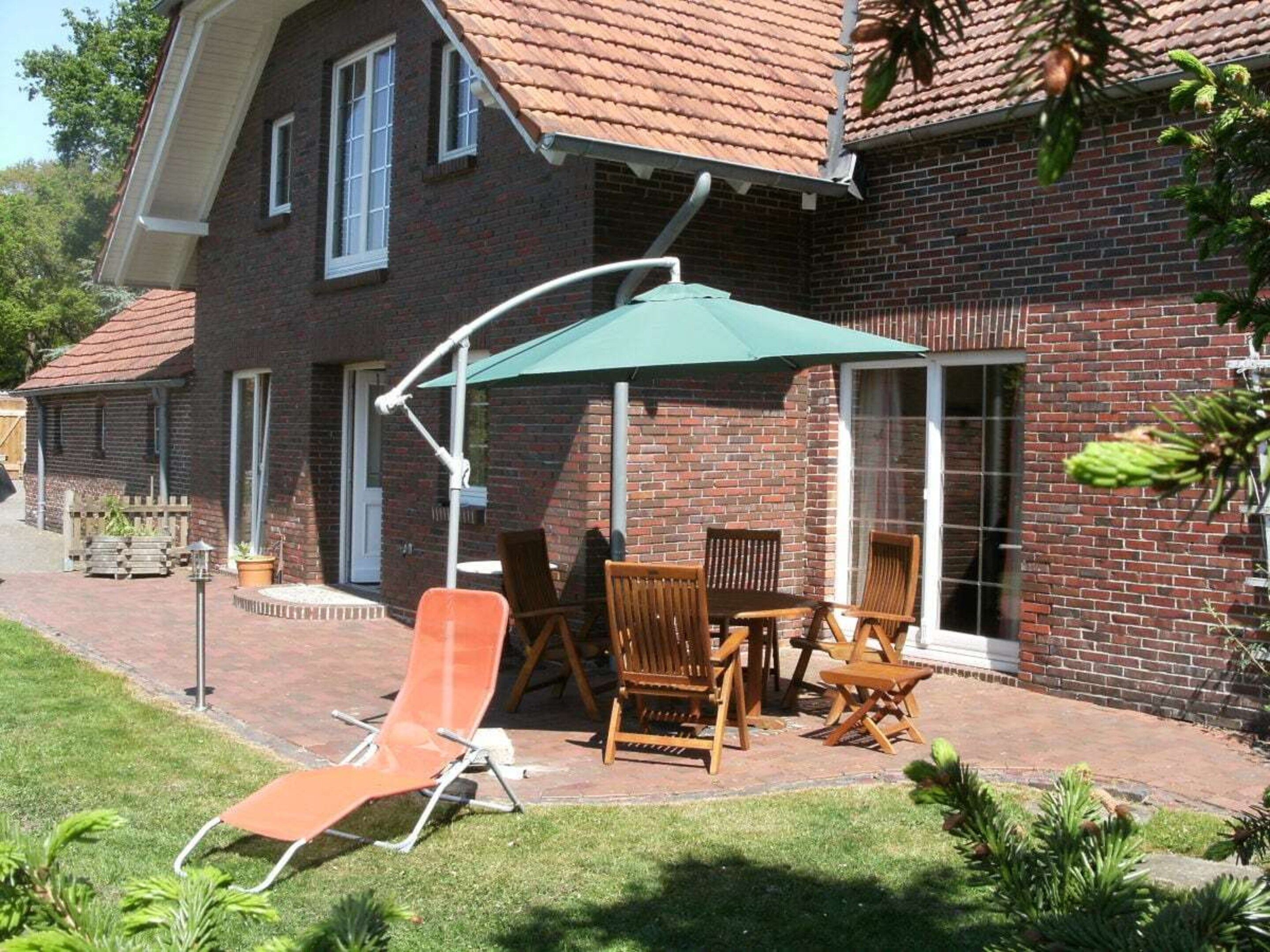 Ein Ziegelhaus mit einer Terrasse, die Gartenmöbel und einen grünen Sonnenschirm zeigt.
