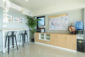 Una zona de recepción limpia y moderna con un mostrador de madera, dos taburetes negros, una planta en maceta, un mapa en la pared y un dispensador de agua.