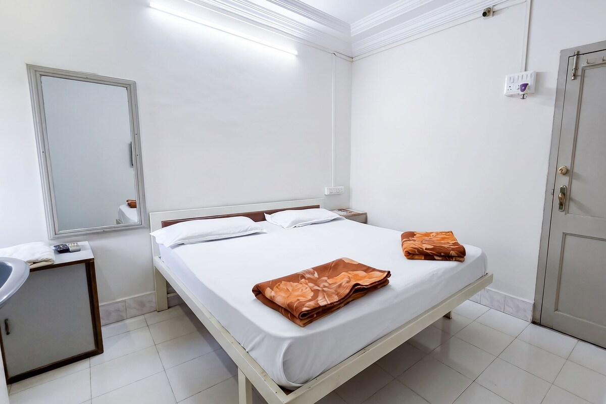 A hotel room with a bed, a bedside table, a mirror, a wardrobe, and a bathroom with a sink.