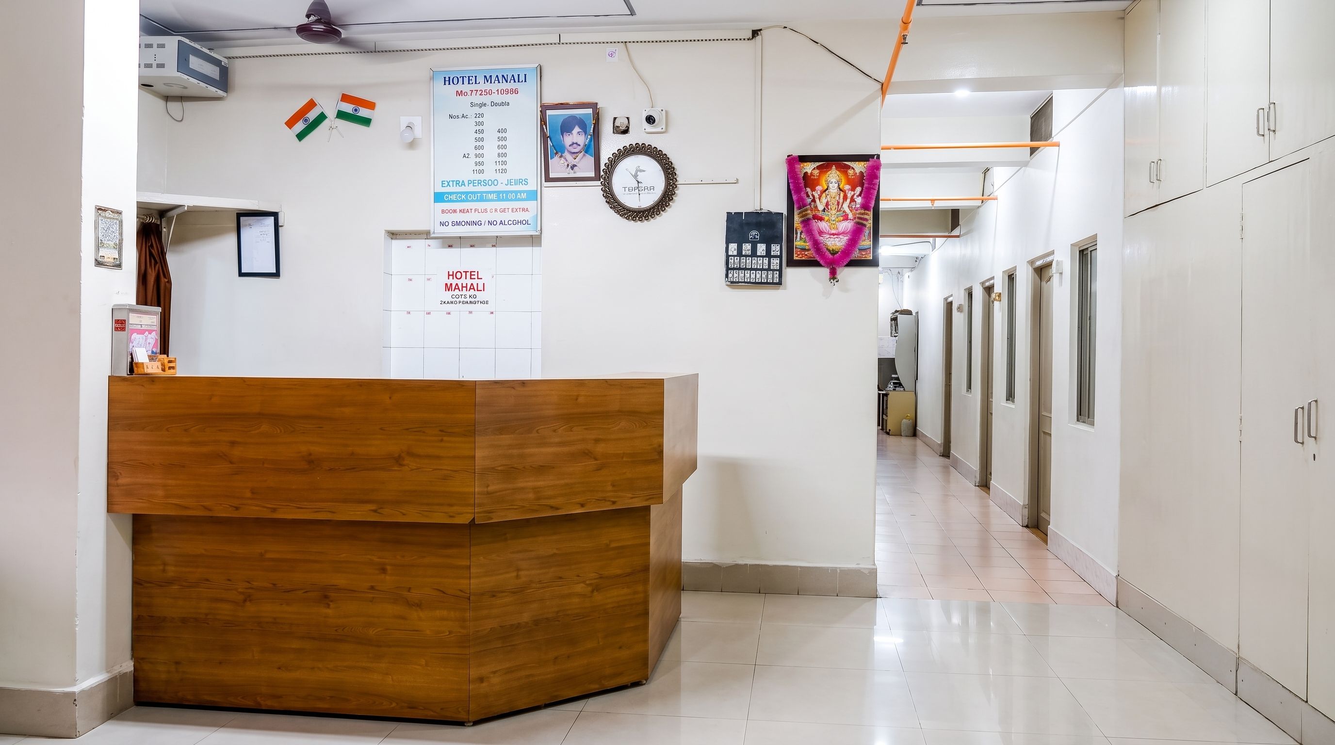 A hotel reception area with a wooden desk, a clock, and a signboard with room rates.
