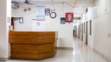 A hotel reception area with a wooden desk, a clock, and a signboard with room rates.