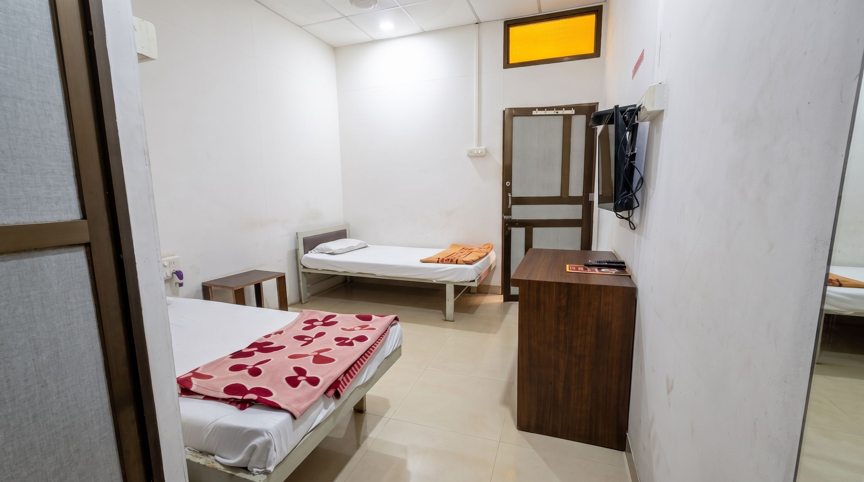 A hotel room with a bed, a bedside table, a small table, a mirror, and a wardrobe.
