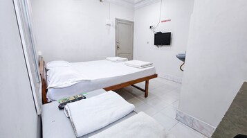 Una habitación pequeña y limpia con una cama individual, una mesita de noche, un televisor y un lavamanos.