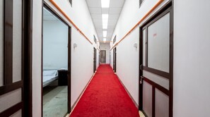 A corridor with a red carpet, doors on both sides, and a bed at the end.