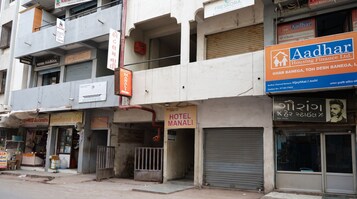 Un edificio de varios pisos con diversos comercios, incluyendo un hotel llamado 'HOTEL MANALI' y una compañía de financiamiento de viviendas llamada 'Aadhar'.