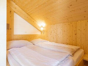 A bedroom with two beds, wooden walls, a sloped ceiling, and a wall-mounted light fixture. - One-bedroom Cabin (Sankt Georgen am Kreischberg)