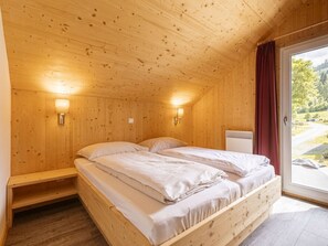 A wooden room with a bed, two wall-mounted lights, and a window with a view of the outdoors. - One-bedroom Cabin (Sankt Georgen am Kreischberg)