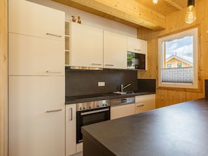 A modern kitchen with white cabinets, a black countertop, and a window with a view of a house. - One-bedroom Cabin (Sankt Georgen am Kreischberg)