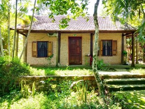 Una pequeña casa de ladrillo con techo de tejas, una puerta de madera y una ventana con persianas.