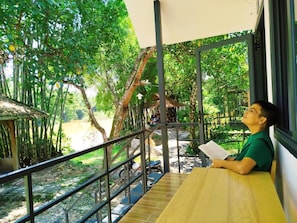 Una persona sentada a una mesa con vista a un paisaje natural, que incluye árboles y un sendero.