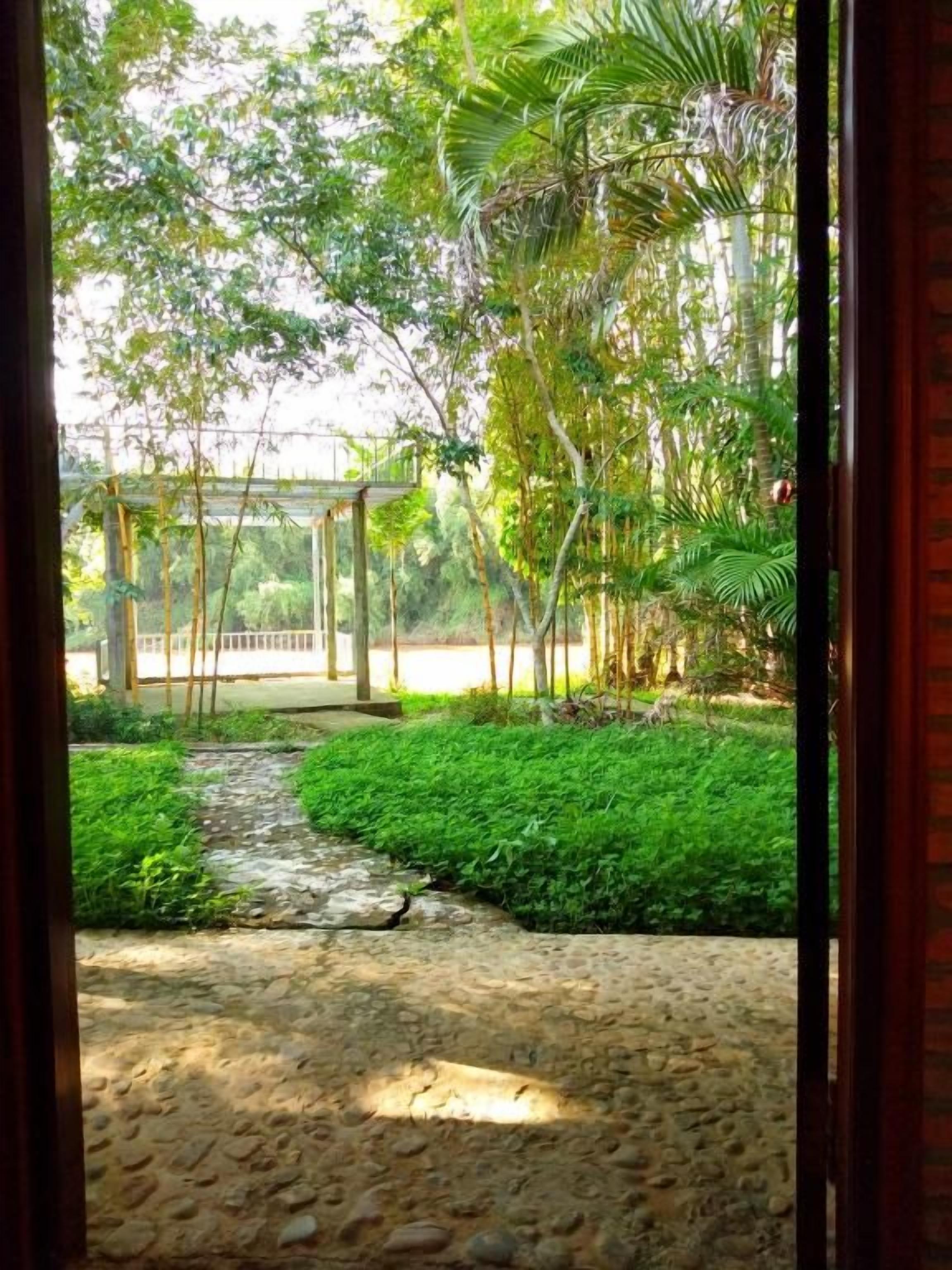 Un sendero de piedra conduce a una pérgola de madera en un jardín exuberante.