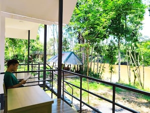 A person seated at a table with a view of a natural landscape, including trees and a water body.