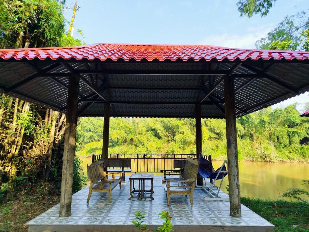 Un espacio de estar al aire libre techado, con piso de baldosas, mobiliario de madera y vistas a un río.