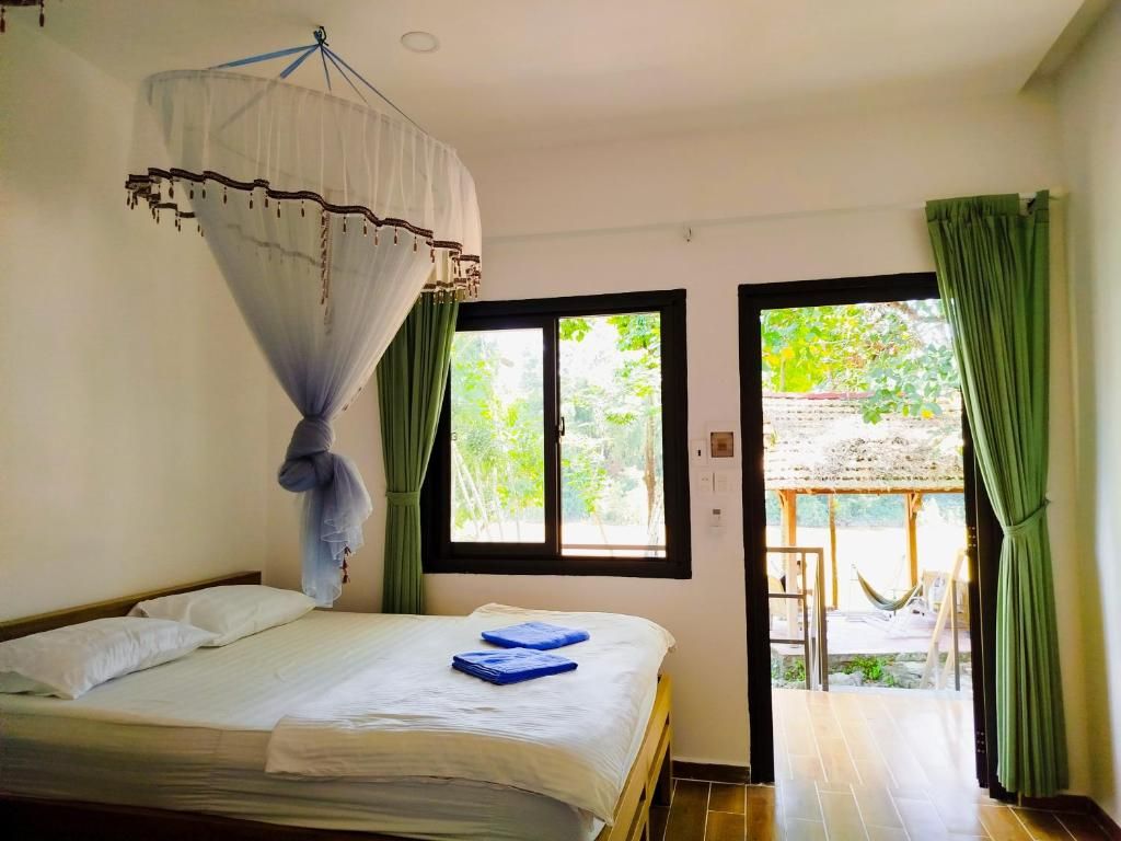 Une chambre avec un lit, une moustiquaire et une vue sur un espace extérieur doté d’une structure en chaume.