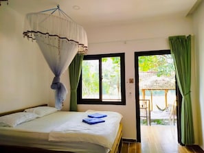 A bedroom with a bed, a mosquito net, and a view of an outdoor area with a thatched structure.