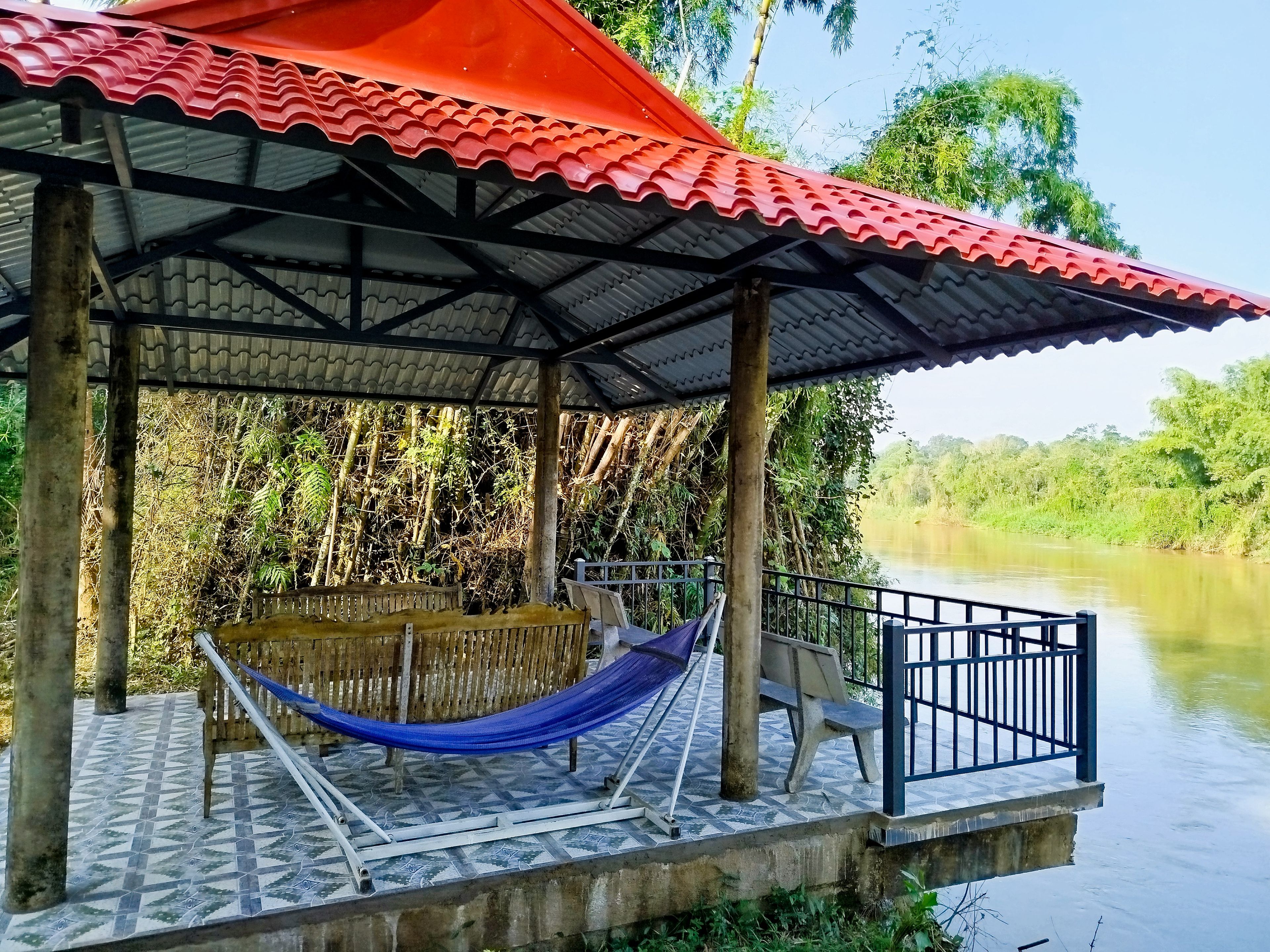 Un espace extérieur abrité, équipé d’un hamac, d’un banc et d’une rambarde donnant sur une rivière.