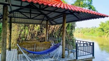 Un espace extérieur abrité, équipé d’un hamac, d’un banc et d’une rambarde donnant sur une rivière.