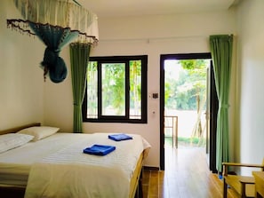 A bedroom with a bed, two windows, a door leading to a balcony, and a chair.