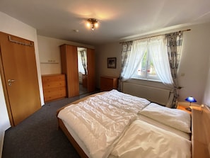 A bedroom with a bed, a wardrobe, a dresser, a window with curtains, and a ceiling light. - Holiday Apartment Seehund – Arrive. Unwind. Enjoy the Sea. (Schönberg (Holstein))