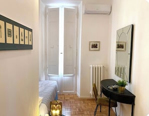 A narrow hallway with a bed, a table with a chair, and a radiator. - Vrbo Property (roma)