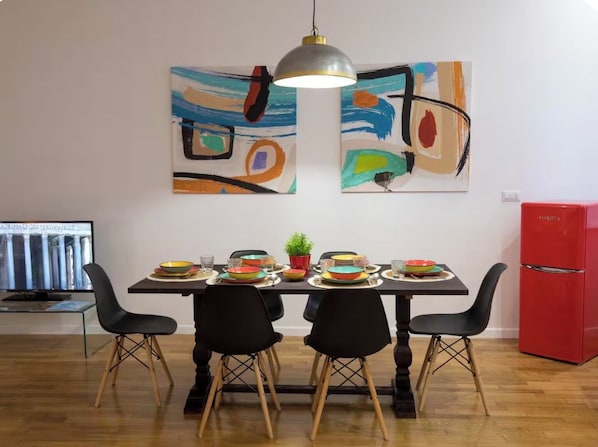 A dining area with a table set for four, surrounded by black chairs, a red refrigerator, and abstract paintings on the wall. - Vrbo Property (roma)